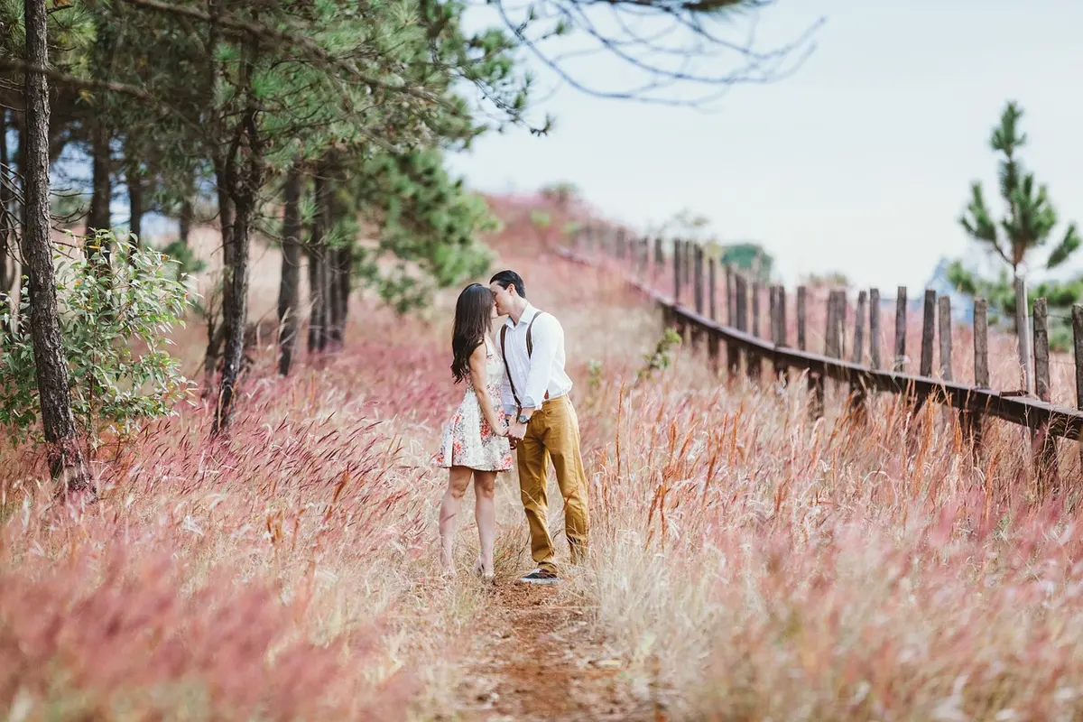 A couple sitting close together outdoors in a sunny setting, smiling at each other with vacation scenery in the background, evoking romance and travel