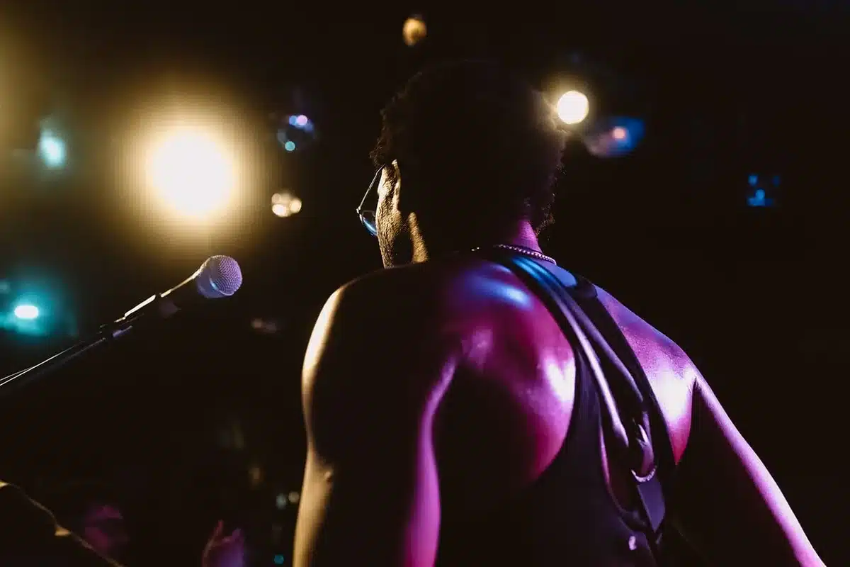 Young male actor on stage in period costume, dramatic spotlight illuminating his face against dark background, Shakespearean tragedy atmosphere