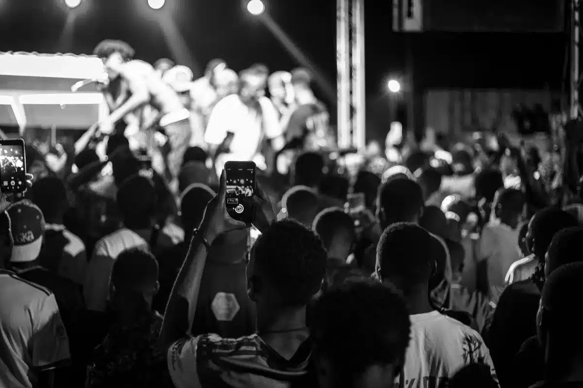 Crowd of anonymous social media users viewing phones, laughing and sharing memes in a dim living-room setting