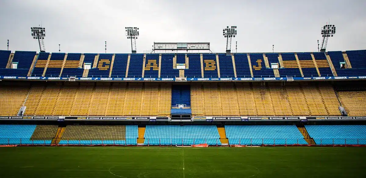 Stadium crowd in the stands wearing blue and yellow colors, hands raised in celebration moment, evening match lighting