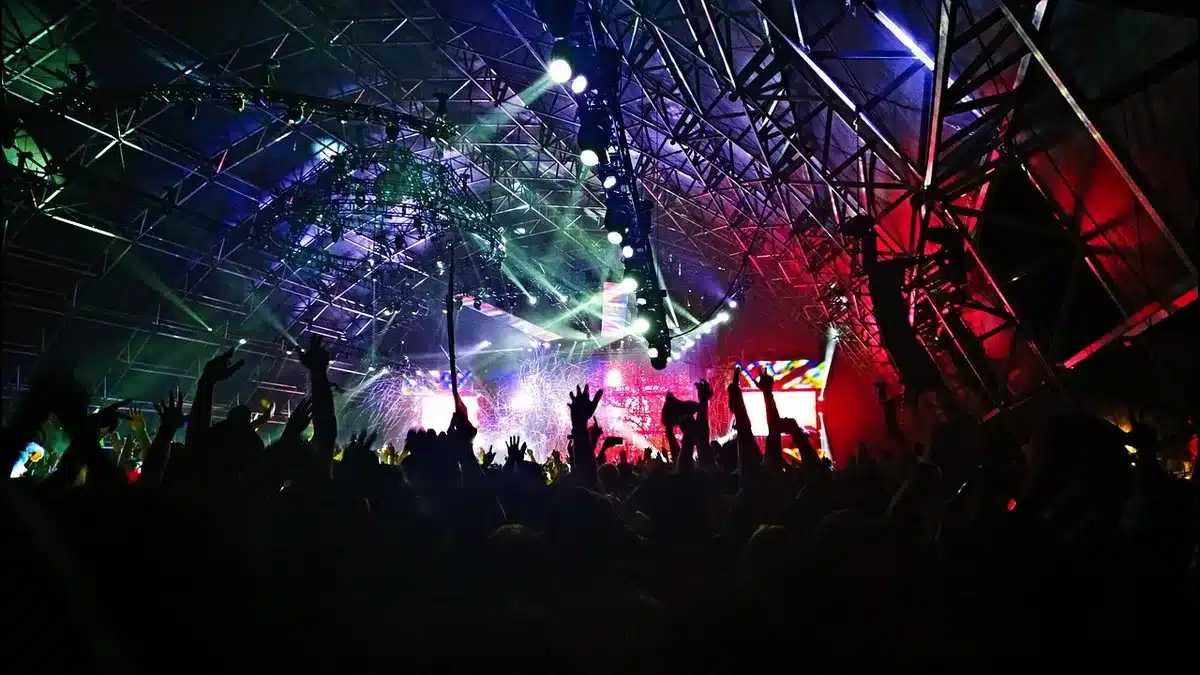 Outdoor festival stage with storm clouds gathering overhead, dramatic dark sky, empty stage under warning lighting, tension in the atmosphere