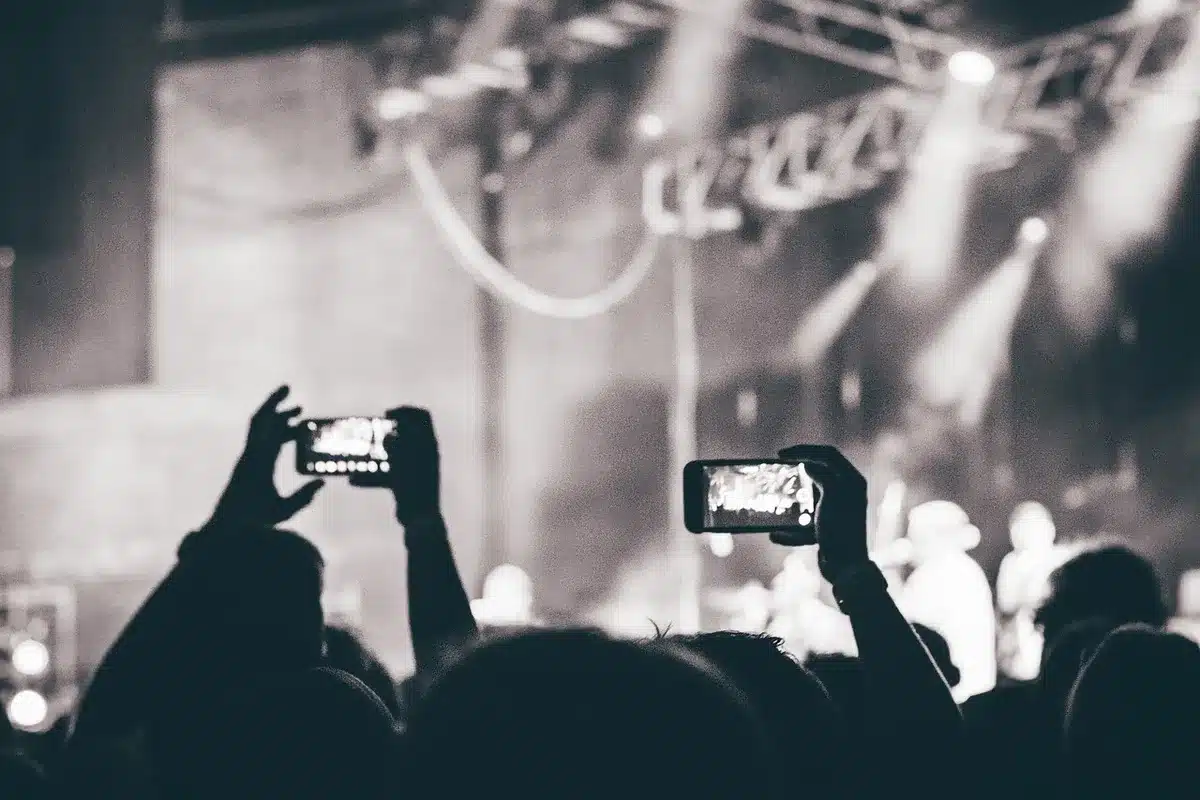 Concert crowd silhouettes against stage lights, anticipation and energy captured, anonymous fans in motion, festival atmosphere