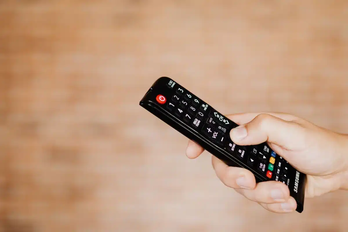 anonymous hands holding a remote control pointed at a blank living room TV, dimmed lights, no identifiable faces
