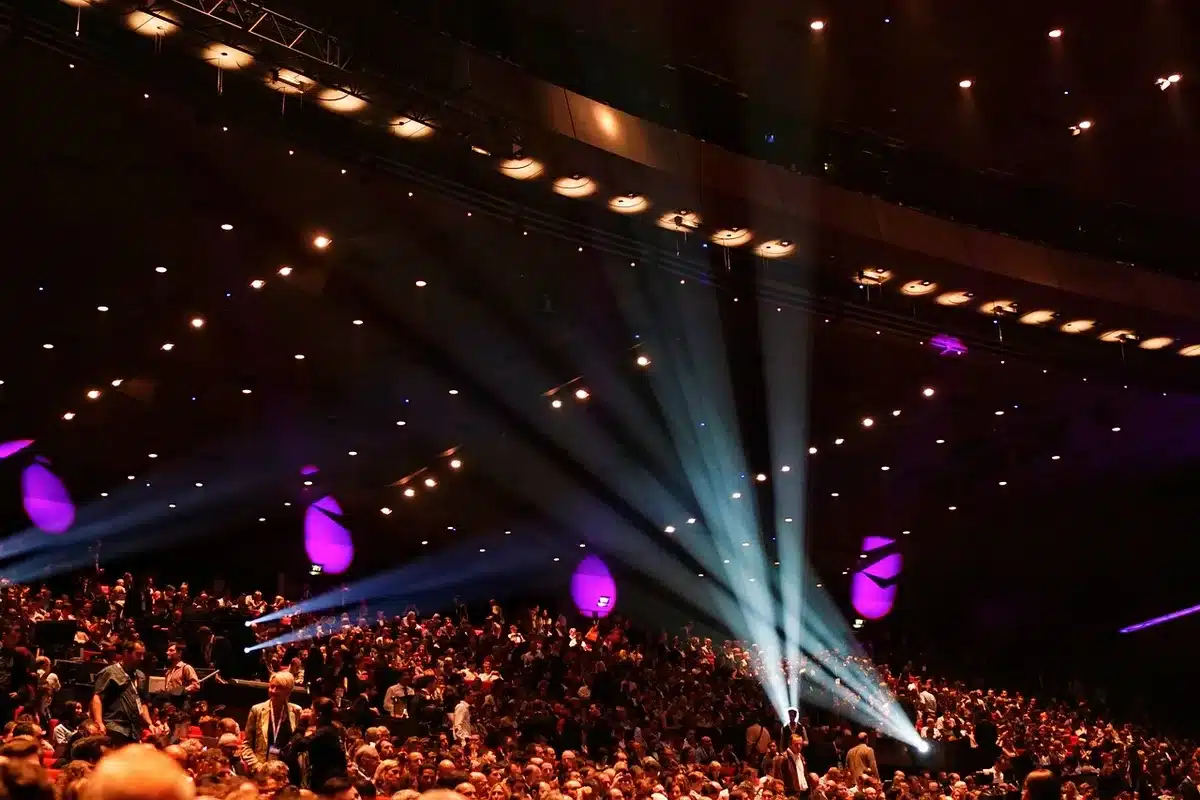 Festival crowd with raised arms silhouetted against stage lights, diverse audience enjoying live music, energy and movement captured mid-performance
