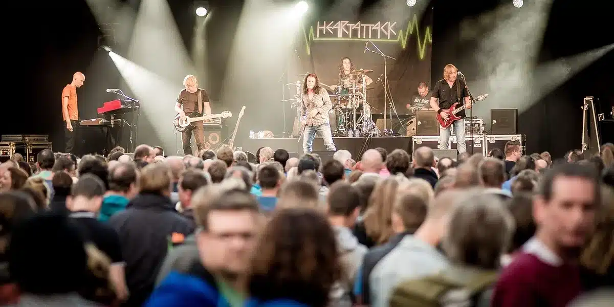 Multidão de fãs em um festival de música ao ar livre sob luzes de palco, braços levantados, energia coletiva visível, com estruturas de palco ao fundo contra o céu noturno