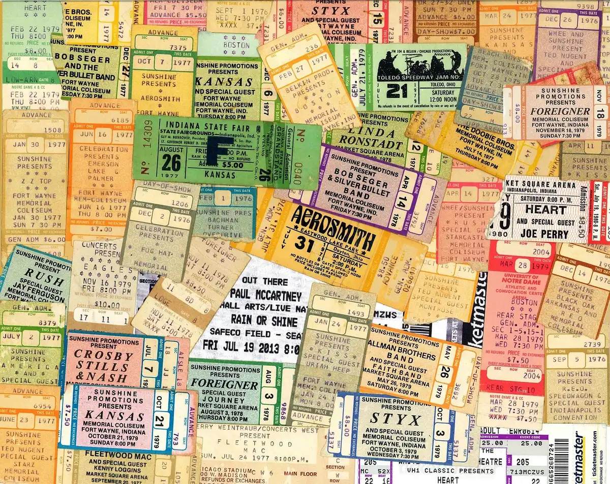 Close-up of anonymous hands holding printed festival tickets and a phone showing an online ticket page, blurred background crowd