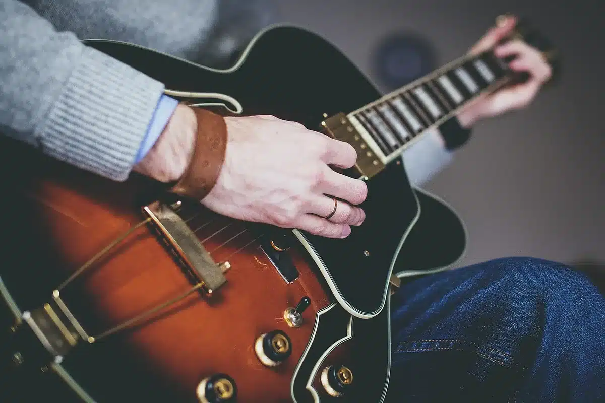 Empty outdoor stage with a lone acoustic guitar on a stool under a single spotlight, no people, festival banners out of focus