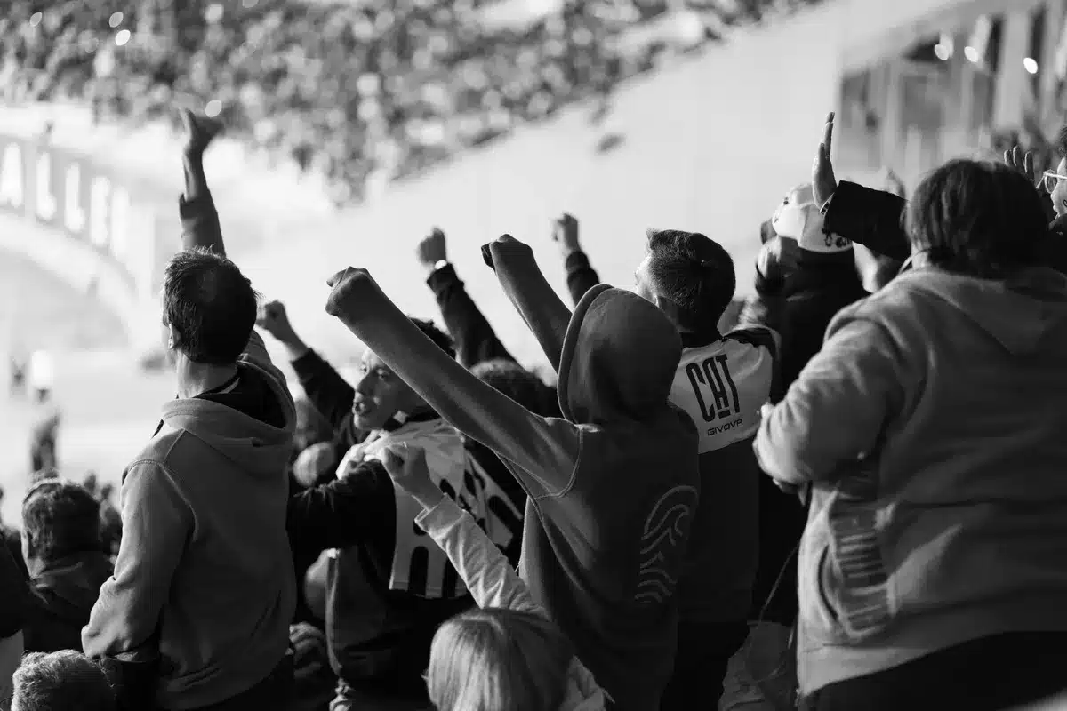 Crowd of anonymous reality-show fans watching live on multiple phones, blurred faces and raised hands in stadium-style seating