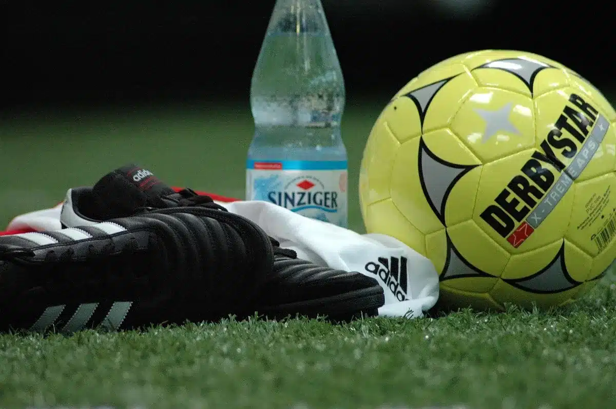 Close-up of a generic football on wet pitch near sideline, anonymous boot in background, empty stands blurred