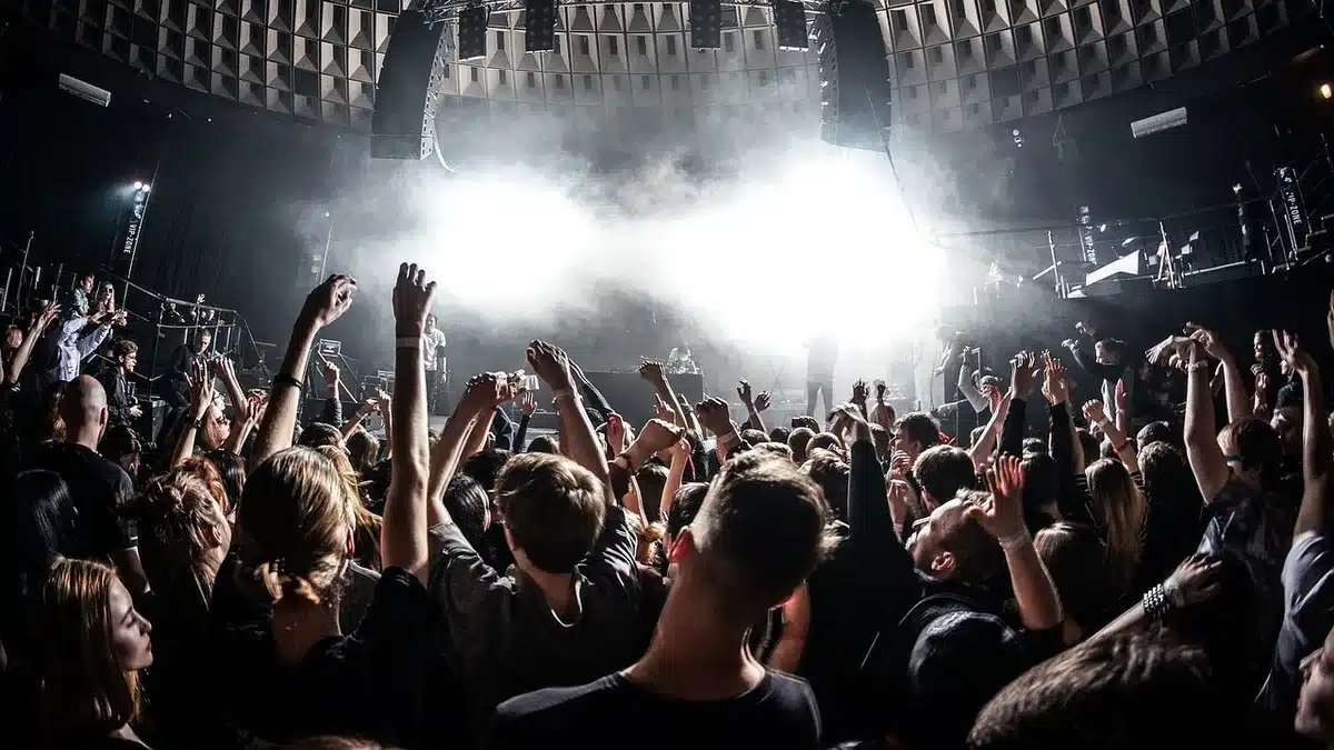 Empty festival stage with an unbranded microphone under warm spotlight, scattered confetti on the floor, distant anonymous silhouettes behind barriers