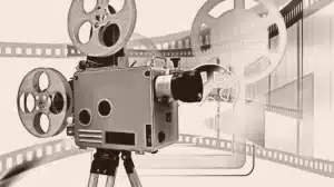 Mãos anônimas segurando um rolo de filme e um clapperboard sobre uma mesa com roteiro ao fundo