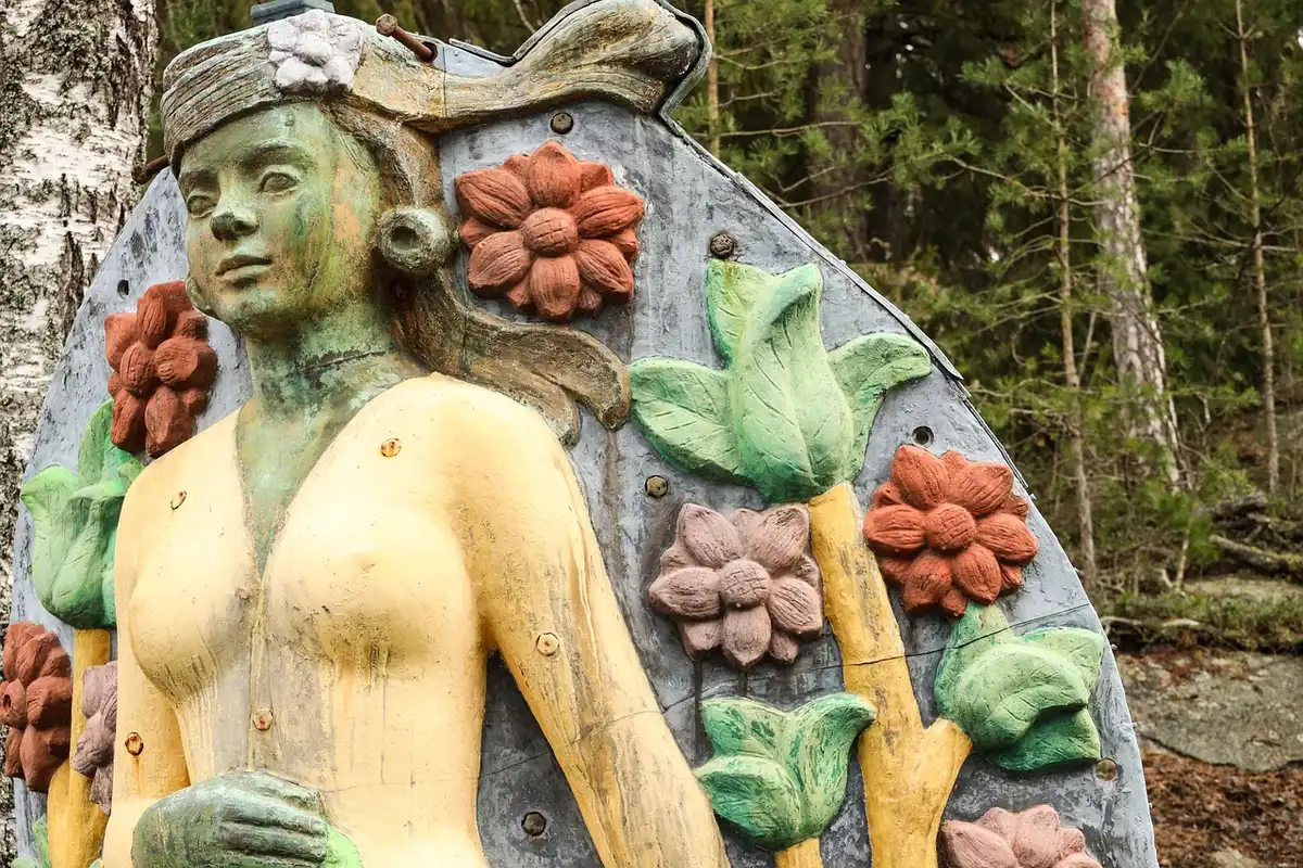 Close-up of unbranded sculpture on plinth in outdoor garden setting, blurred people in background