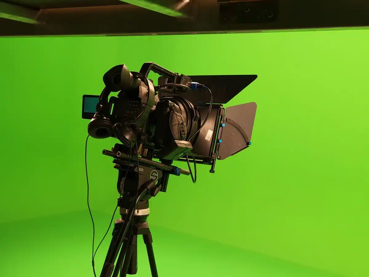 Empty studio desk under studio lights, single anonymous microphone on a stand, cameras and blurred crew in background