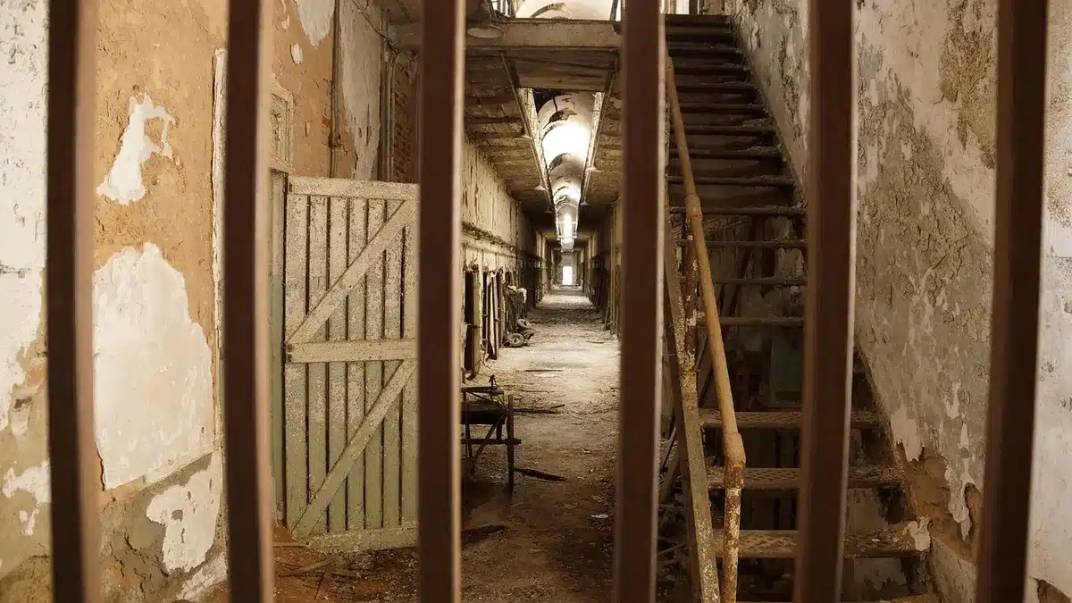 Empty prison corridor with a single distant light, a closed cell door and a folded legal document on a bench