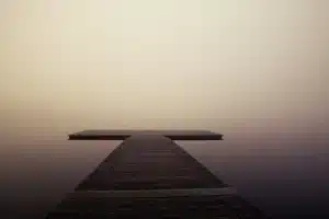 Margem de lago enevoada ao anoitecer com um cais de madeira vazio e uma bota vermelha na areia