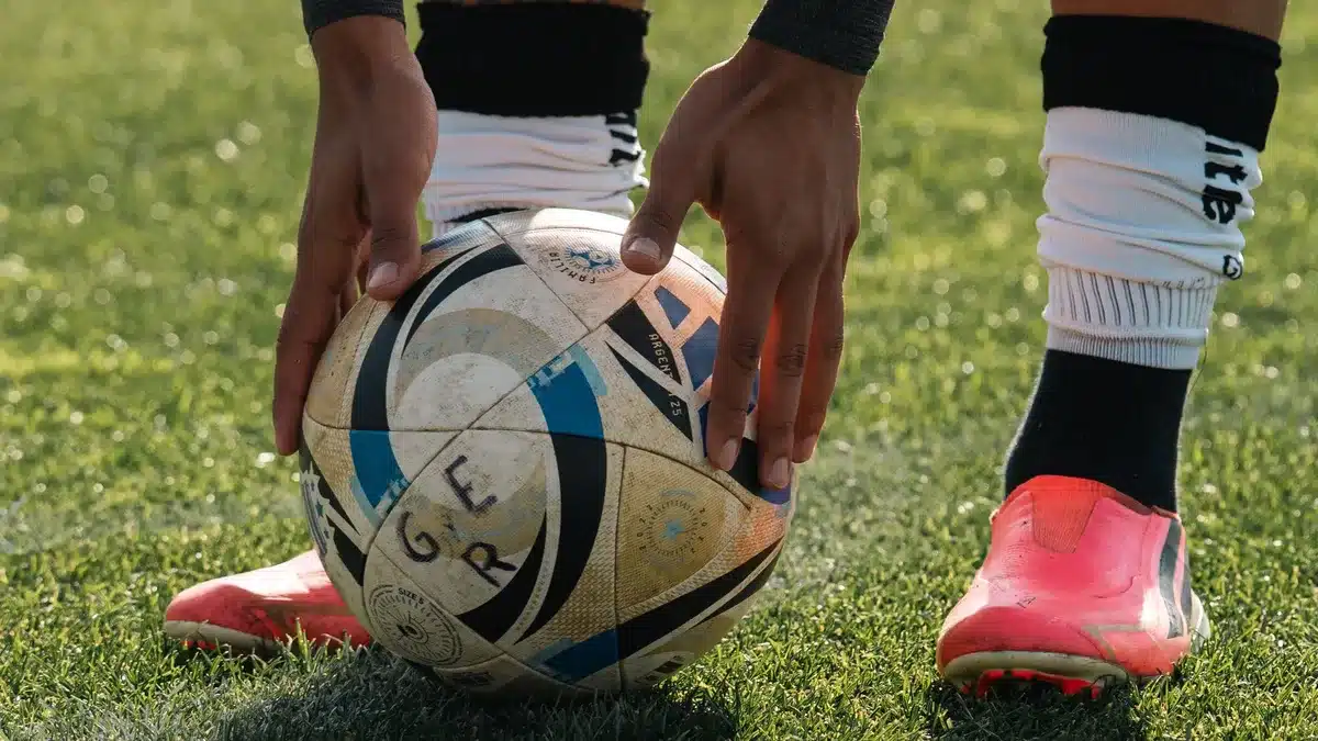Close-up of a generic pair of football boots beside an unbranded training bib on grass
