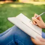 Mãos anônimas sobre caderno antigo e caneta em um estúdio, janela e mansão ao fundo