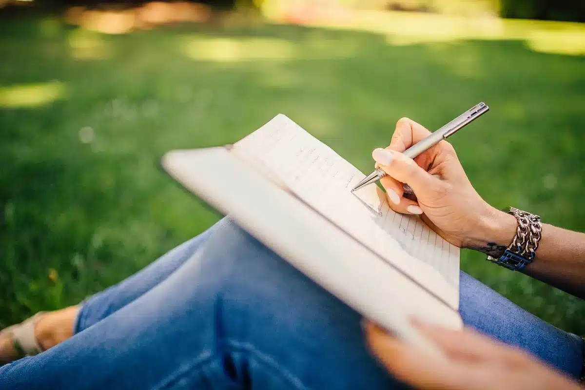 Mãos anônimas sobre caderno antigo e caneta em um estúdio, janela e mansão ao fundo